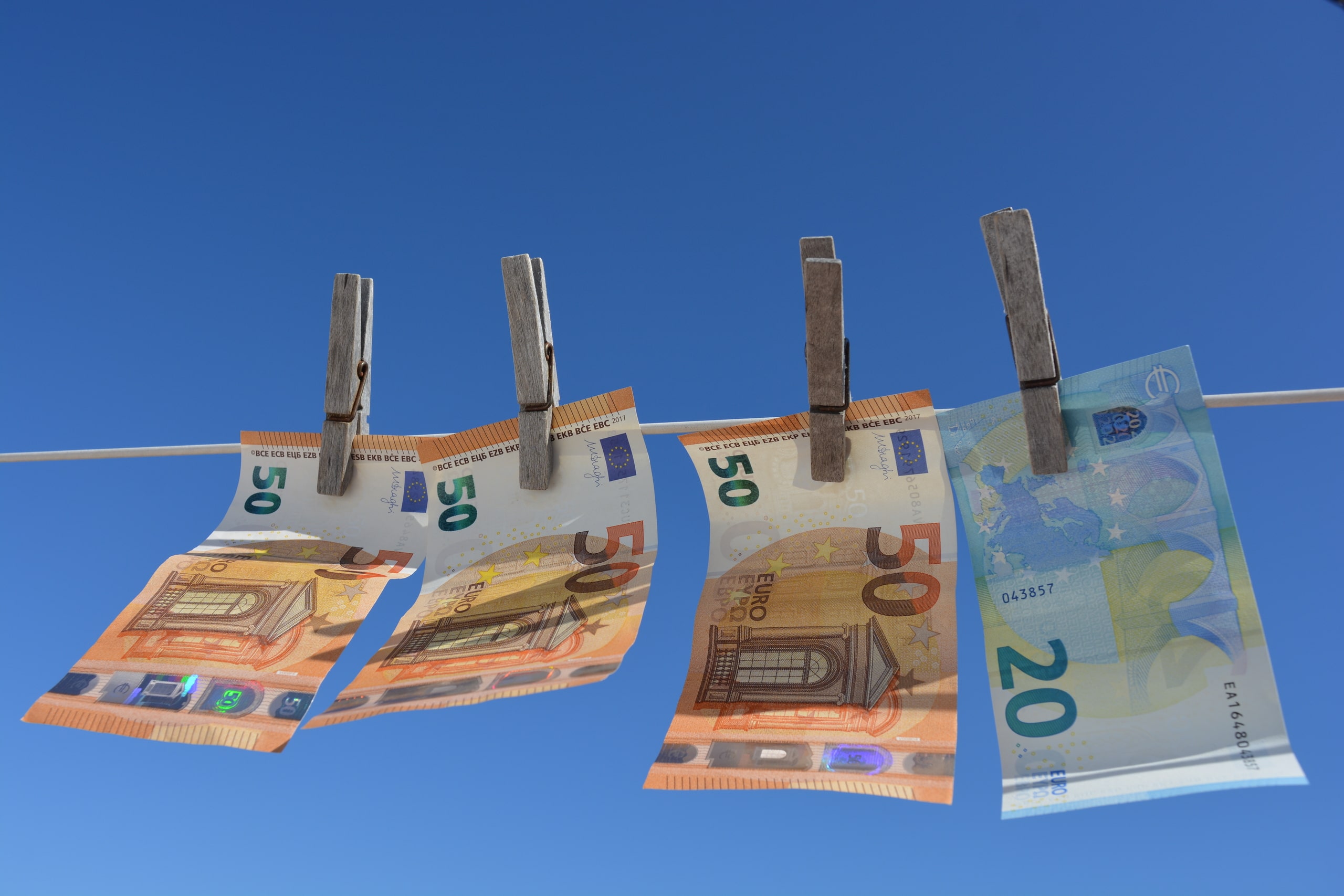 Euros Colgados Como Prevención Al Blanqueo De Capitales Billetes de 50 y 20 euros sujetados con pinzas en una cuerda contra un cielo despejado, representando la transparencia en la auditoría y prevención de blanqueo de capitales.