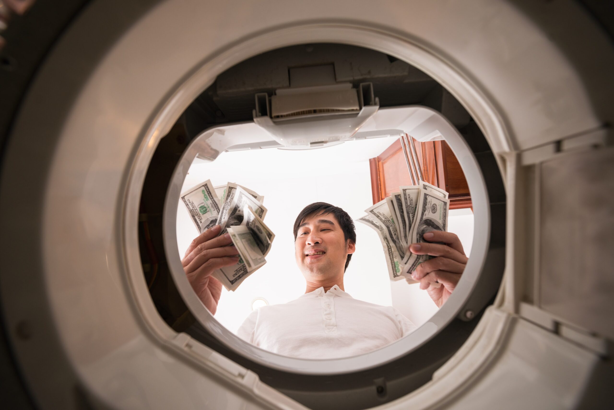 Blanqueo De Capitales En Entidades Financieras Representado Con Metáfora De Lavado De Dinero Hombre sosteniendo fajos de billetes en lo que parece ser la puerta de una lavadora, simbolizando el blanqueo de capitales en el contexto de entidades financieras.