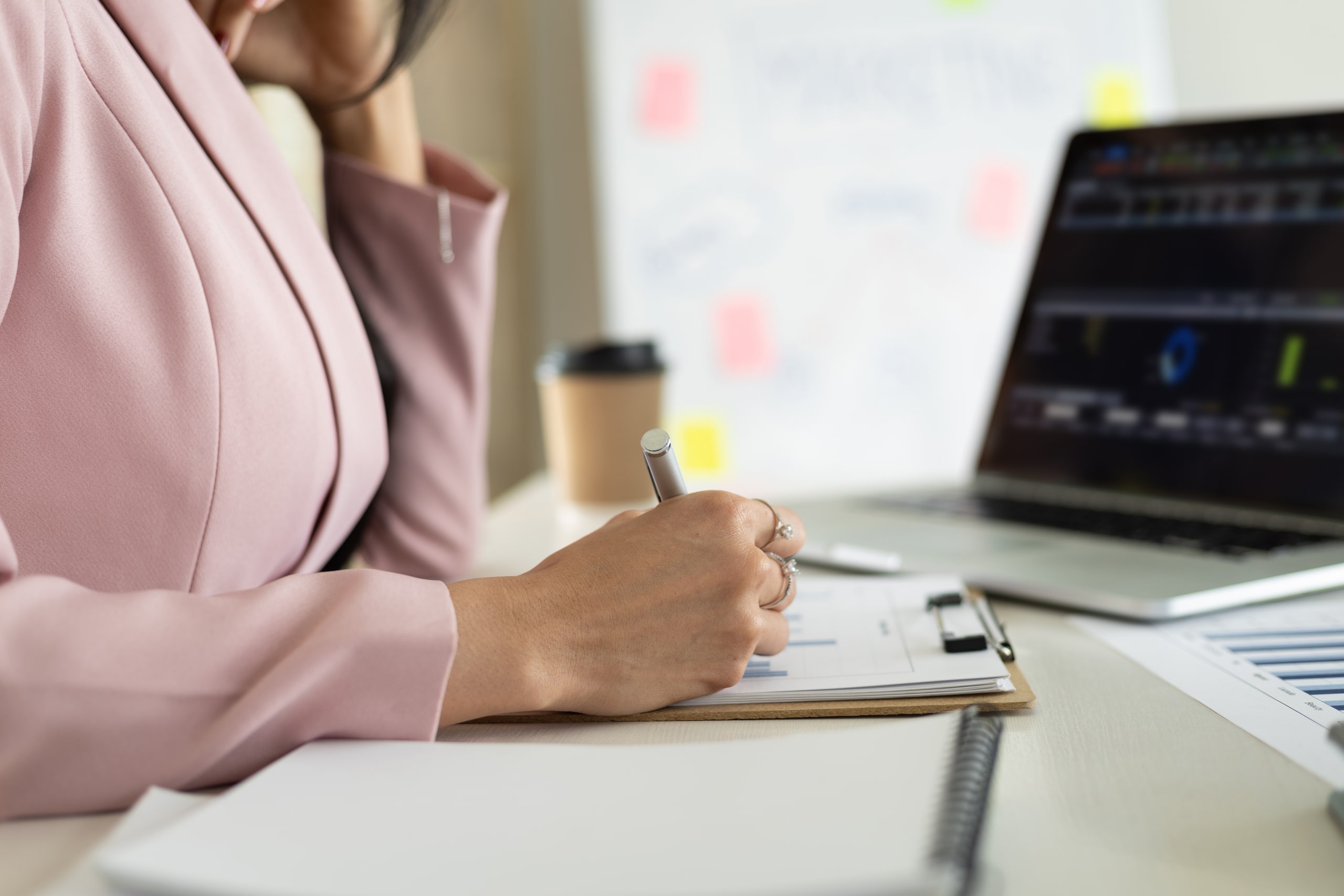 Profesional Realizando Análisis De Riesgos Financieros En Entorno De Oficina Persona en traje rosado trabajando en análisis de riesgos financieros frente a un portátil en la oficina, con gráficos y documentos.