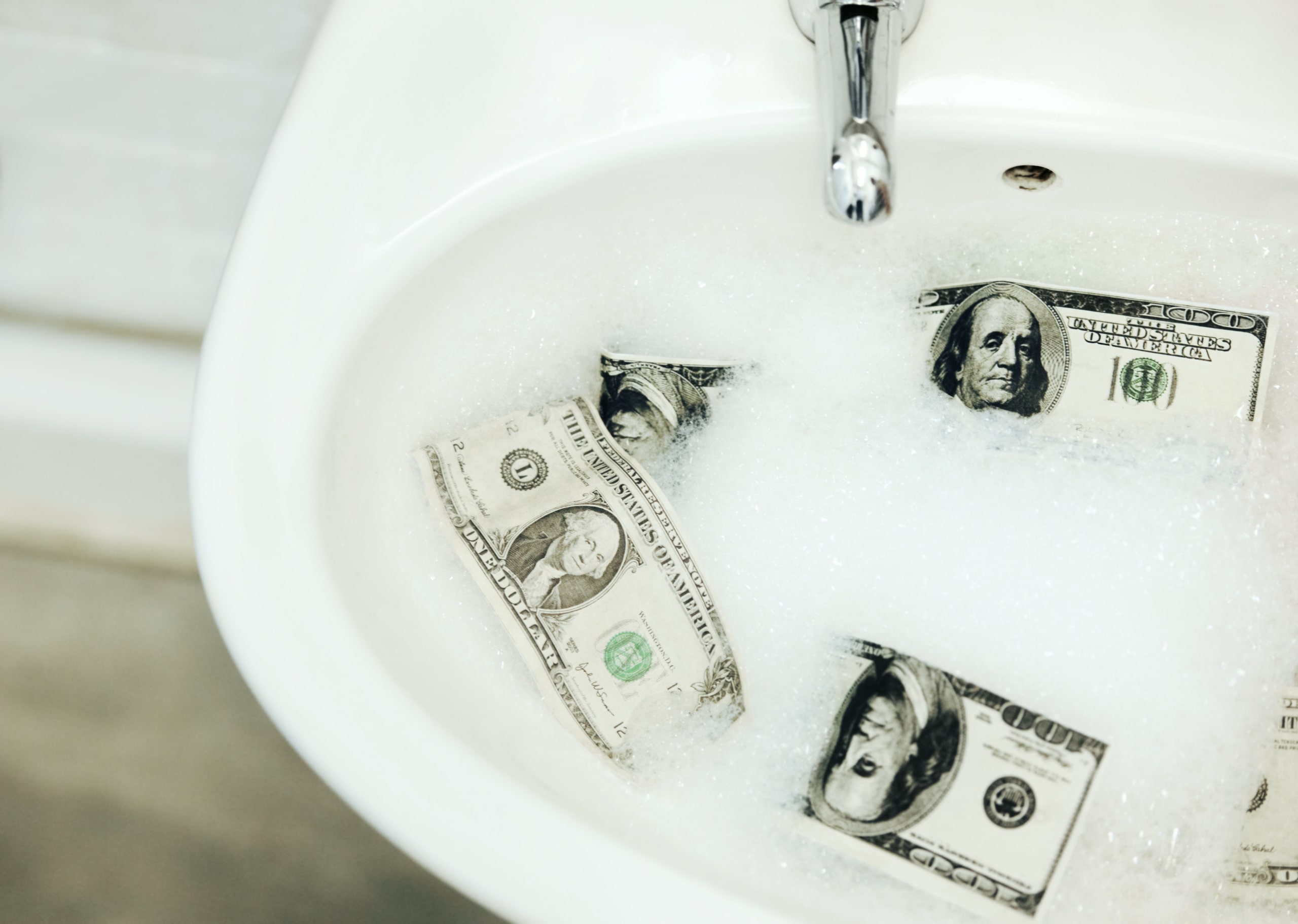 Importancia De La Auditoría Forense En La Prevención Del Blanqueo De Capitales Billetes de dólares en un lavabo con espuma, representando el concepto de blanqueo de capitales y la necesidad de auditoría forense para combatir actividades financieras ilícitas.