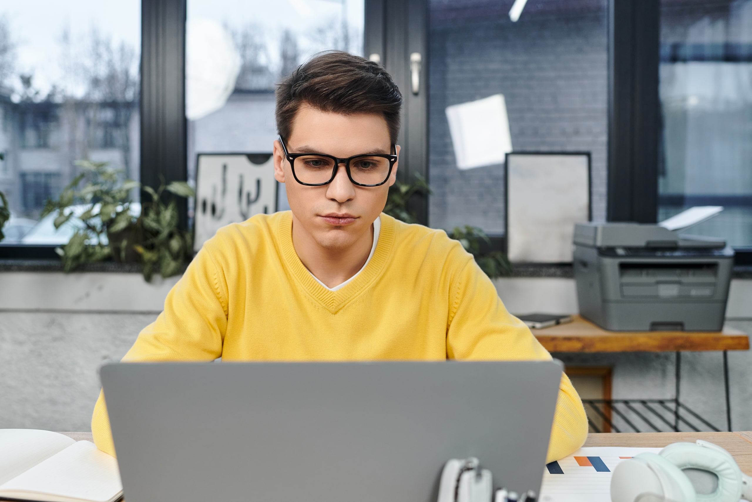 Programas De Capacitación En Prevención De Blanqueo De Capitales Persona joven con gafas trabajando en un ordenador portátil en una oficina moderna, lo que representa la importancia de los programas de capacitación en la prevención del blanqueo de capitales.