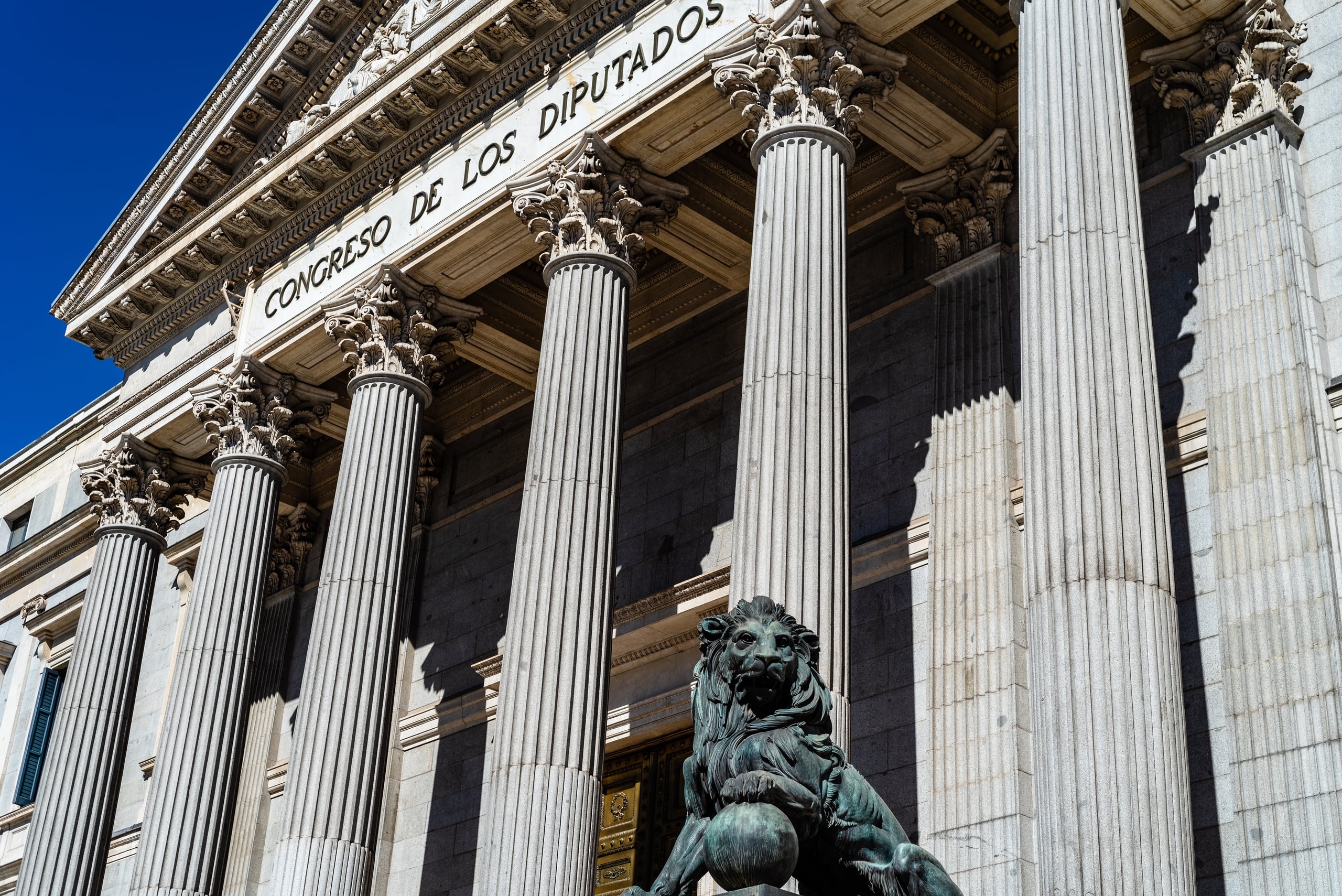 Ministerio De Economía Y Empresa Sede Institucional Y Marco Legislativo En España Fachada de un edificio institucional con grandes columnas clásicas y una escultura de león frente a la entrada, representando la sede del Ministerio de Economía y Empresa y el marco legislativo económico en España.